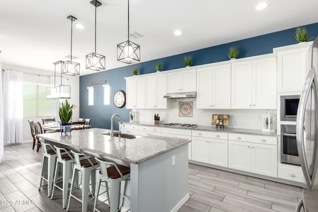 kitchen featuring a kitchen island with sink, a sink, appliances with stainless steel finishes, white cabinetry, and tasteful backsplash