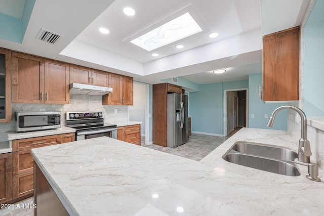 kitchen featuring backsplash, sink, a skylight, light stone countertops, and appliances with stainless steel finishes