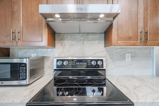 kitchen with light stone countertops, stainless steel appliances, tasteful backsplash, and range hood