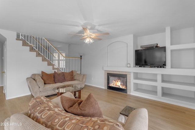 living room with a tile fireplace, wood finished floors, baseboards, built in features, and stairway