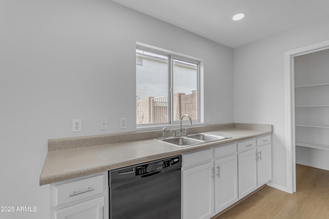 kitchen featuring black dishwasher, light countertops, light wood-style flooring, white cabinetry, and a sink