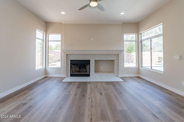 unfurnished living room featuring ceiling fan, a healthy amount of sunlight, light wood-type flooring, and a tiled fireplace