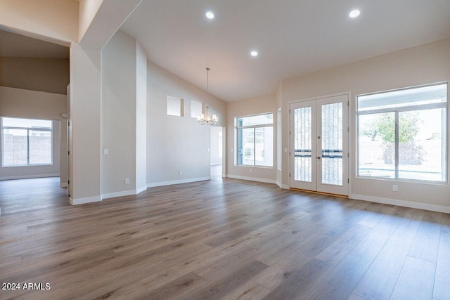 unfurnished room with hardwood / wood-style floors, a notable chandelier, high vaulted ceiling, and french doors