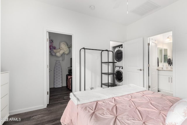 bedroom with visible vents, dark wood-type flooring, a walk in closet, stacked washing maching and dryer, and a closet