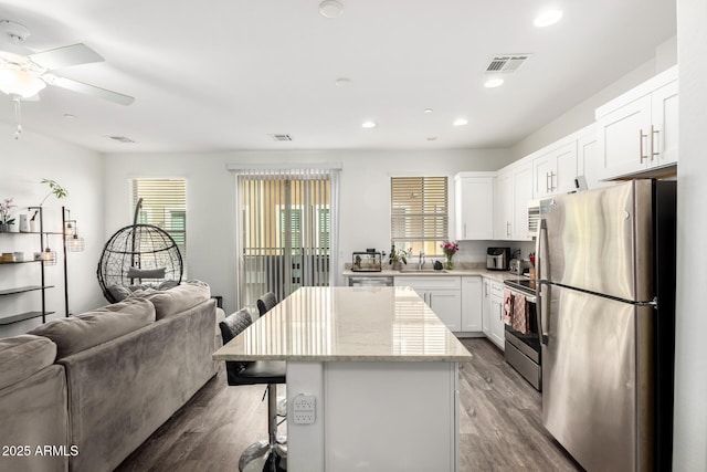 kitchen featuring visible vents, appliances with stainless steel finishes, open floor plan, a kitchen island, and wood finished floors