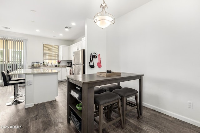 kitchen featuring a breakfast bar, dark wood-style flooring, white cabinets, freestanding refrigerator, and a center island