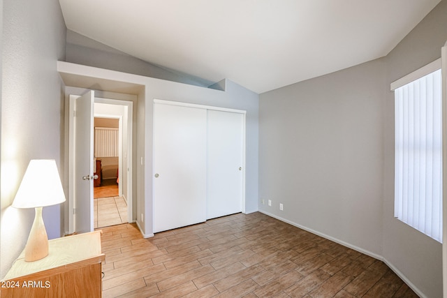 unfurnished bedroom with vaulted ceiling, light hardwood / wood-style flooring, and a closet