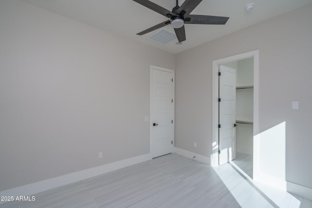 unfurnished bedroom with ceiling fan, a spacious closet, light hardwood / wood-style floors, and a closet