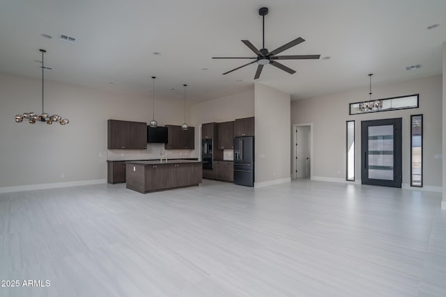 kitchen featuring hanging light fixtures, dark brown cabinets, black appliances, and a center island with sink