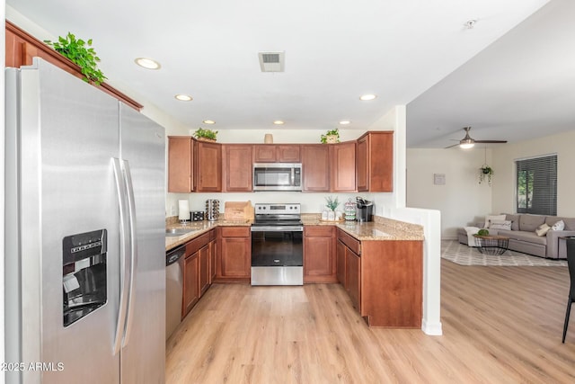 kitchen with light stone countertops, stainless steel appliances, brown cabinets, light wood finished floors, and open floor plan