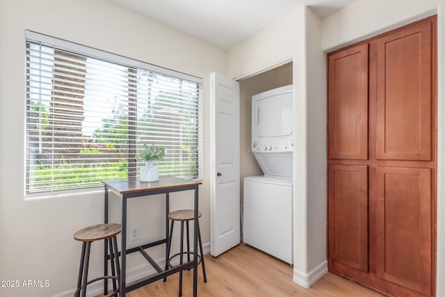 laundry area featuring stacked washer / drying machine, light wood-type flooring, laundry area, and baseboards