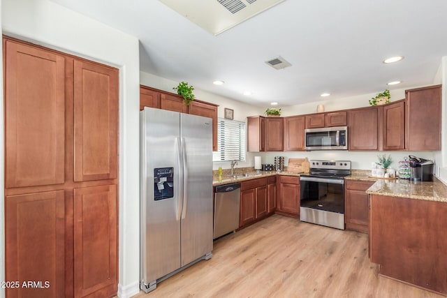 kitchen with light stone countertops, a sink, brown cabinetry, light wood-type flooring, and appliances with stainless steel finishes