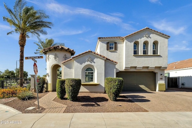 mediterranean / spanish-style home featuring a tile roof, decorative driveway, fence, a garage, and stucco siding
