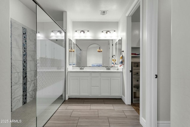 bathroom featuring visible vents, a sink, a walk in shower, and double vanity