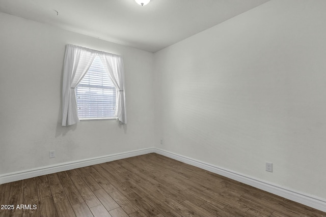 spare room with baseboards and dark wood-type flooring