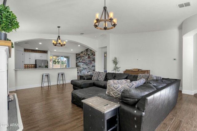 living room featuring arched walkways, dark wood-style flooring, baseboards, visible vents, and an inviting chandelier