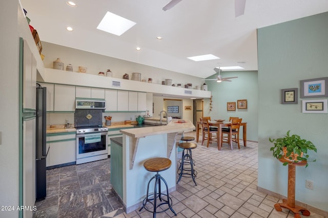 kitchen with a kitchen breakfast bar, a skylight, white cabinets, and appliances with stainless steel finishes