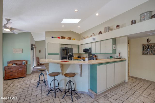 kitchen featuring white cabinetry, ceiling fan, black refrigerator, lofted ceiling with skylight, and a breakfast bar