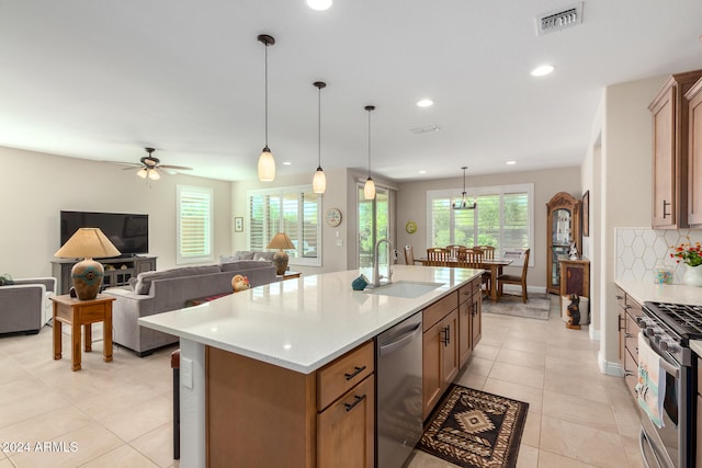 kitchen with an island with sink, stainless steel appliances, sink, pendant lighting, and tasteful backsplash