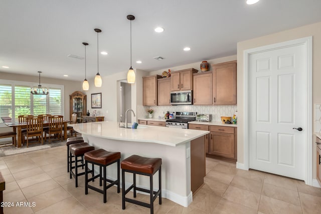 kitchen with stainless steel appliances, a kitchen bar, a chandelier, and a kitchen island with sink