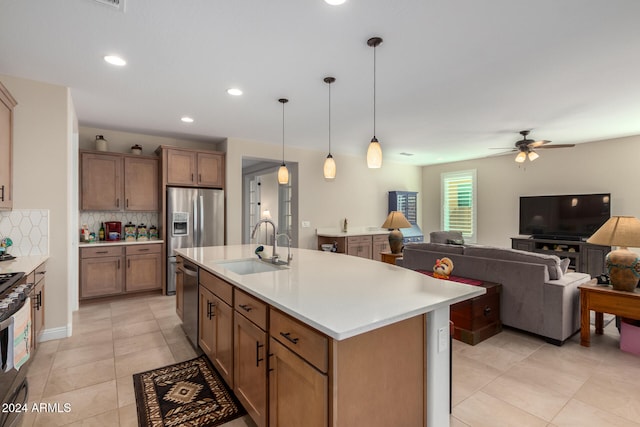 kitchen with tasteful backsplash, appliances with stainless steel finishes, a kitchen island with sink, pendant lighting, and sink