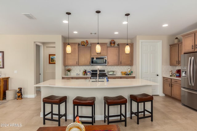 kitchen with a center island with sink, a kitchen breakfast bar, decorative light fixtures, and stainless steel appliances