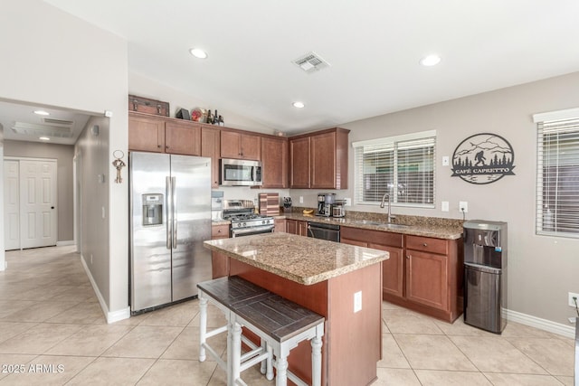 kitchen with sink, a breakfast bar area, a center island, stainless steel appliances, and light stone countertops