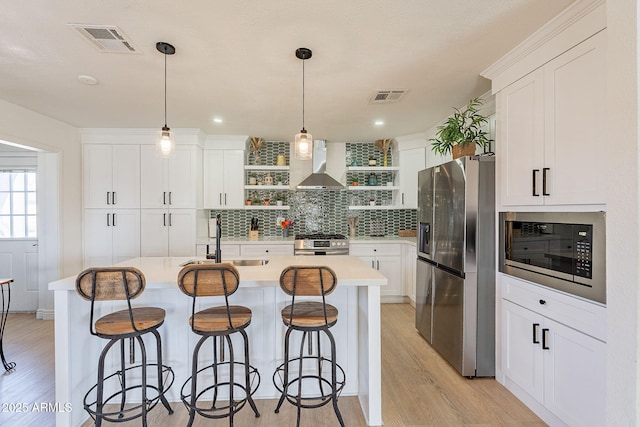 kitchen featuring visible vents, open shelves, appliances with stainless steel finishes, wall chimney exhaust hood, and a sink