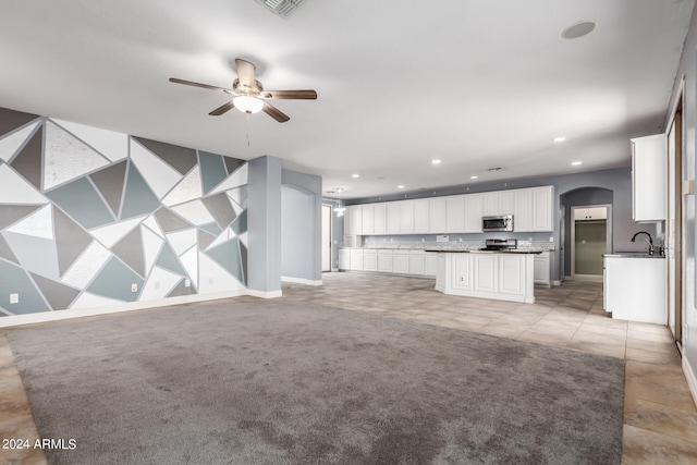 unfurnished living room with ceiling fan, light colored carpet, and sink