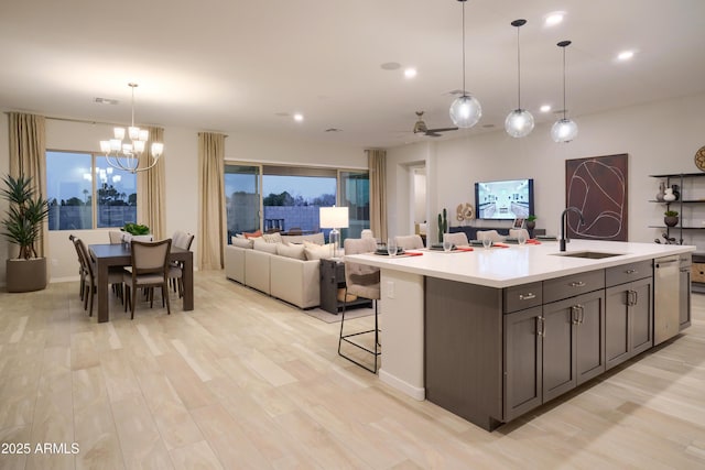 kitchen featuring sink, hanging light fixtures, a center island with sink, ceiling fan with notable chandelier, and light wood-type flooring