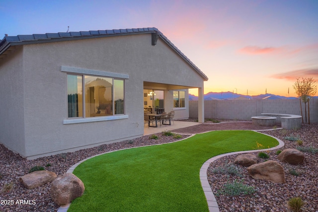 back house at dusk featuring a patio area and a lawn