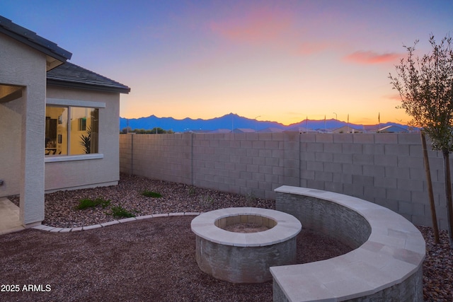 yard at dusk featuring an outdoor fire pit, a mountain view, and a patio