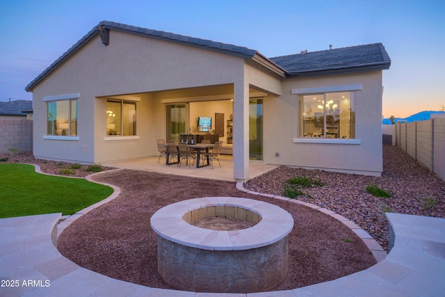 back house at dusk featuring a patio and an outdoor fire pit