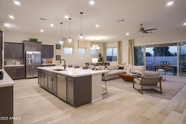 kitchen with sink, dark brown cabinets, appliances with stainless steel finishes, pendant lighting, and a kitchen island with sink