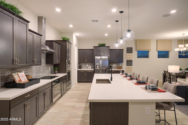 kitchen featuring sink, stainless steel fridge, a kitchen breakfast bar, an island with sink, and wall chimney range hood