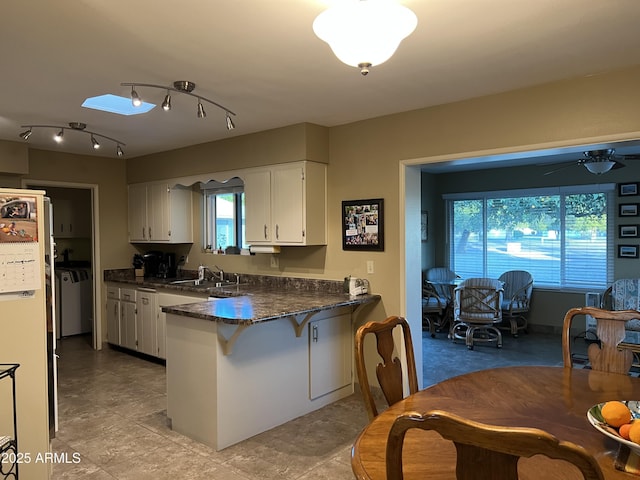 kitchen with white cabinetry, sink, dark stone counters, kitchen peninsula, and washing machine and dryer