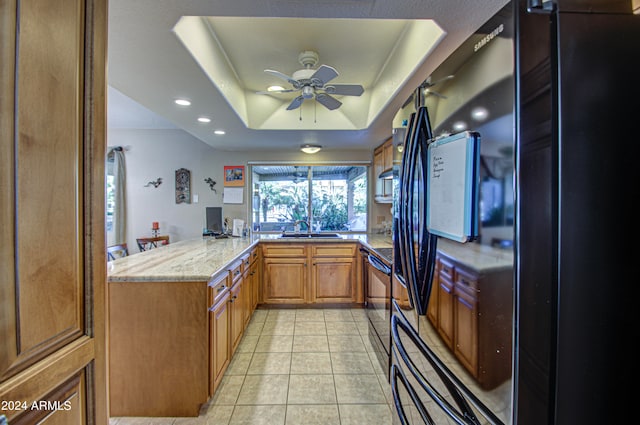 kitchen with black appliances, light stone counters, sink, a tray ceiling, and kitchen peninsula