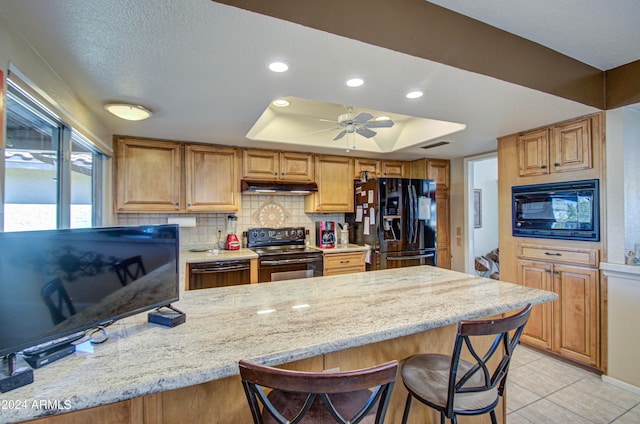 kitchen with black appliances, tasteful backsplash, light stone countertops, a breakfast bar area, and a tray ceiling