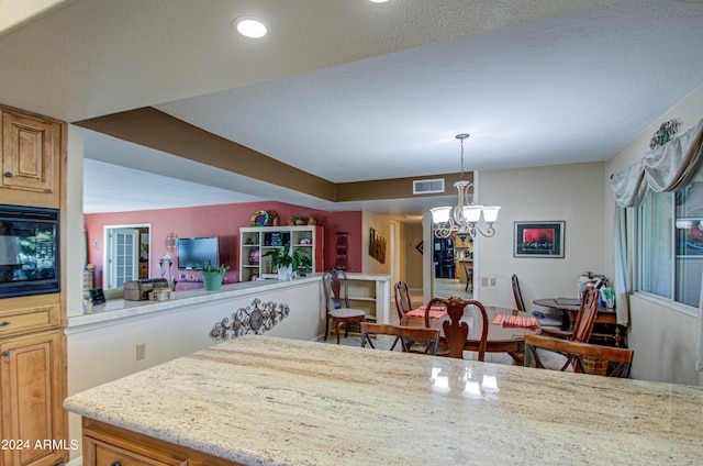 kitchen with light stone countertops, decorative light fixtures, a notable chandelier, and black microwave