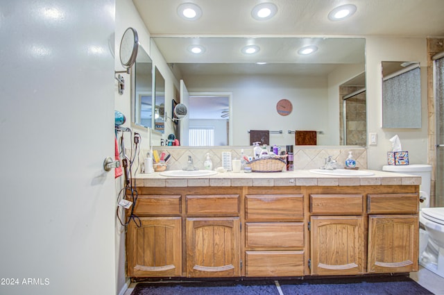 bathroom with toilet, vanity, decorative backsplash, and a shower with shower door