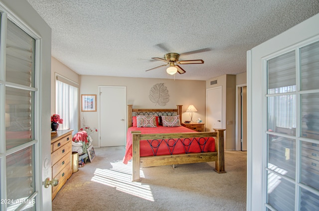 bedroom with multiple windows, a textured ceiling, light colored carpet, and ceiling fan