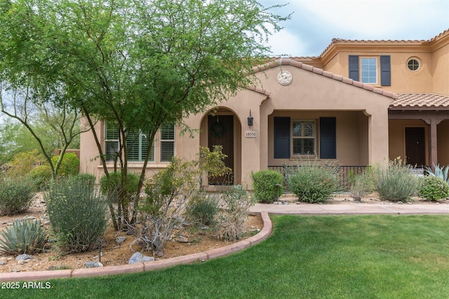 view of front of property featuring a tiled roof, covered porch, a front yard, and stucco siding