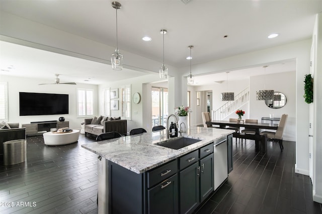 kitchen with stainless steel dishwasher, a sink, dark wood finished floors, ceiling fan, and light stone countertops
