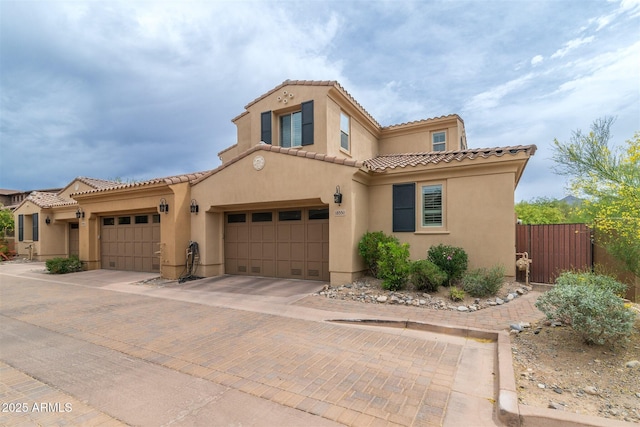 mediterranean / spanish-style house featuring stucco siding, a tile roof, fence, and decorative driveway