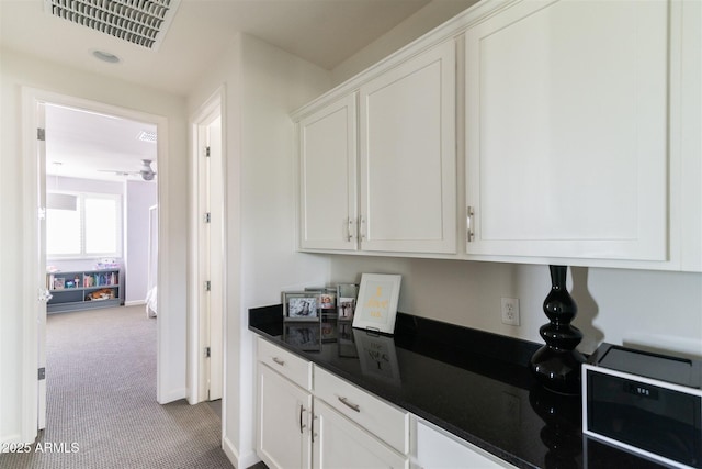 kitchen with white cabinets, dark countertops, visible vents, baseboards, and carpet flooring