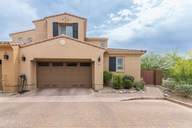 mediterranean / spanish-style home with a garage, driveway, a tiled roof, and stucco siding