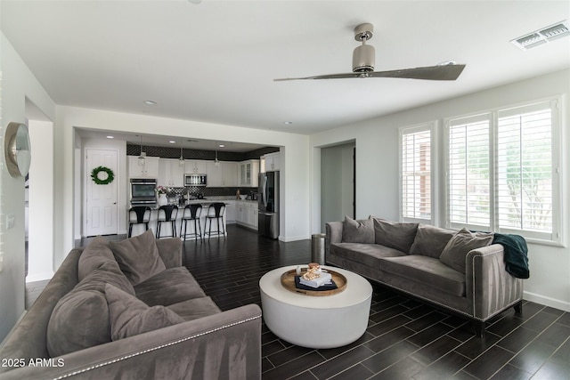 living room featuring a ceiling fan, plenty of natural light, baseboards, wood finish floors, and visible vents