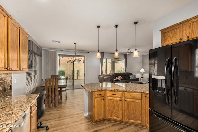 kitchen featuring black fridge, decorative light fixtures, light hardwood / wood-style floors, light stone counters, and a chandelier