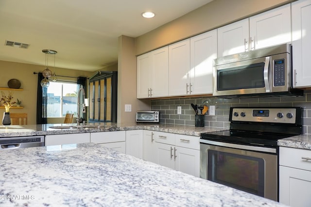 kitchen featuring white cabinets, stainless steel appliances, decorative light fixtures, and backsplash