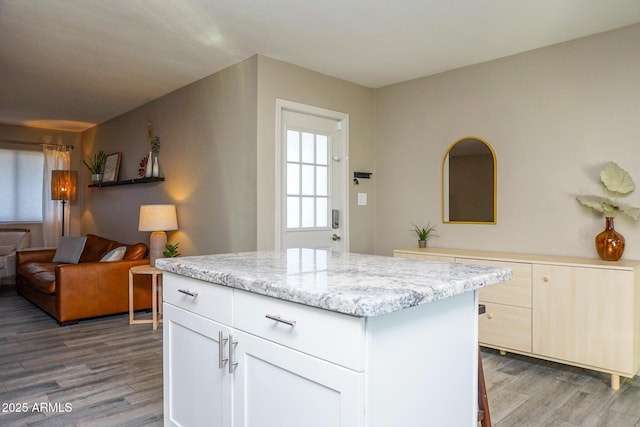 kitchen featuring light stone counters, white cabinets, a kitchen island, and wood-type flooring